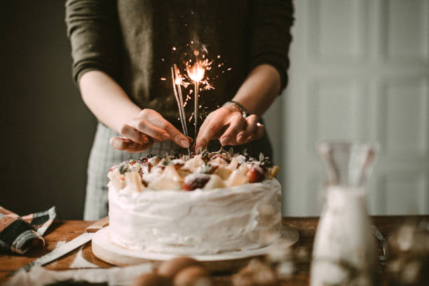 Hands decorating a white birthday cake with sparklers on a wooden table